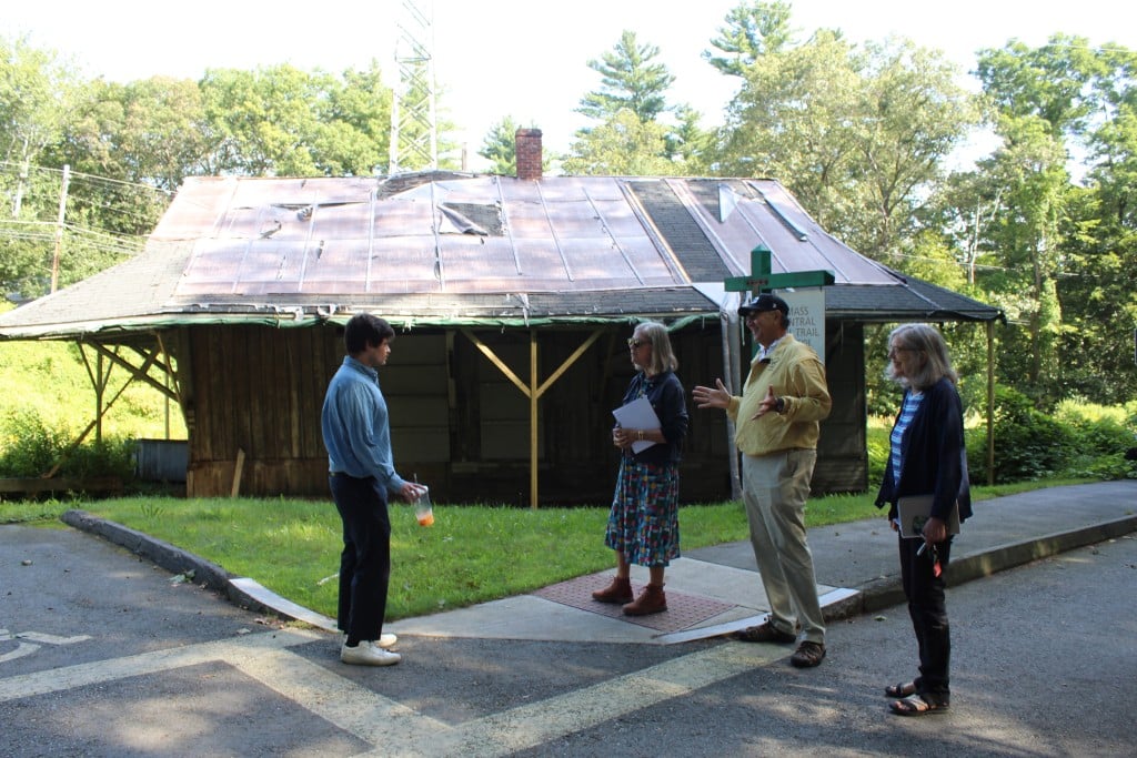 People stand in front of a run-down, historic train depot.